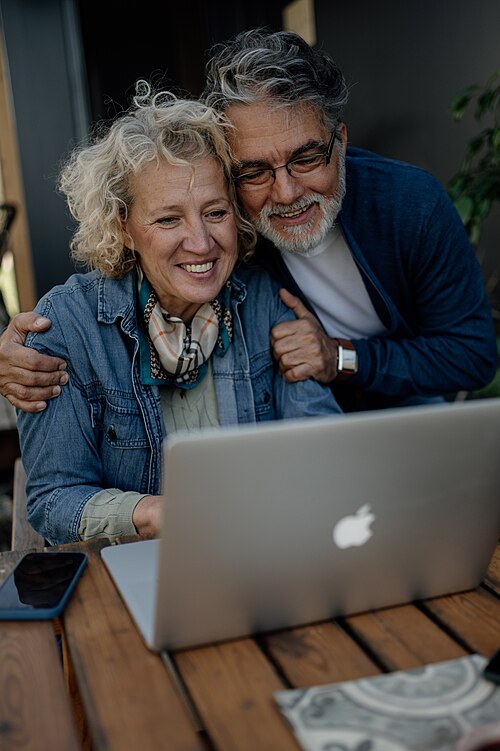 A smiling senior couple sharing a laptop at a garden table